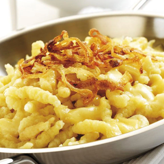 Spätzle topped with browned onion rings in a metal serving pan