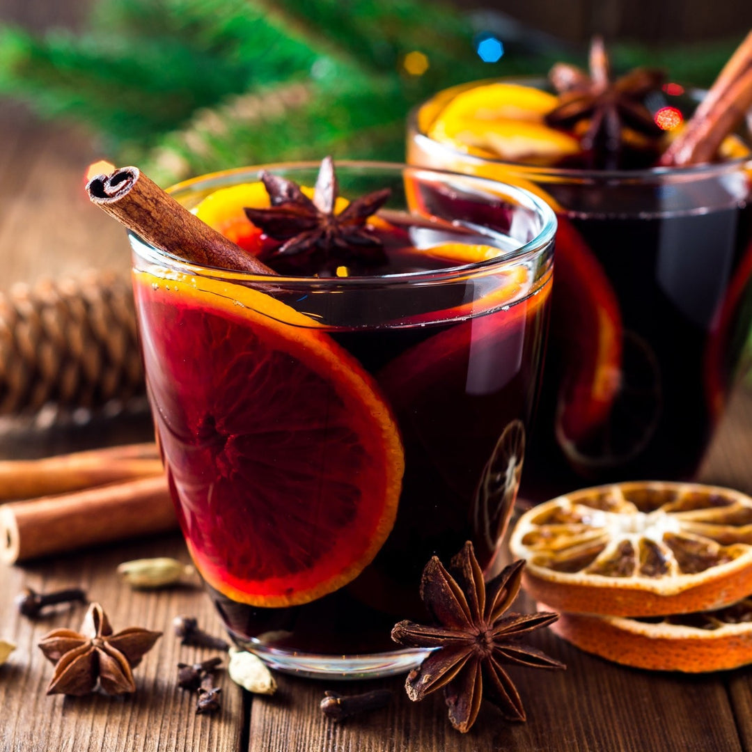 Two glasses of red mulled wine with orange slices, cinnamon sticks and star anise on a wooden table