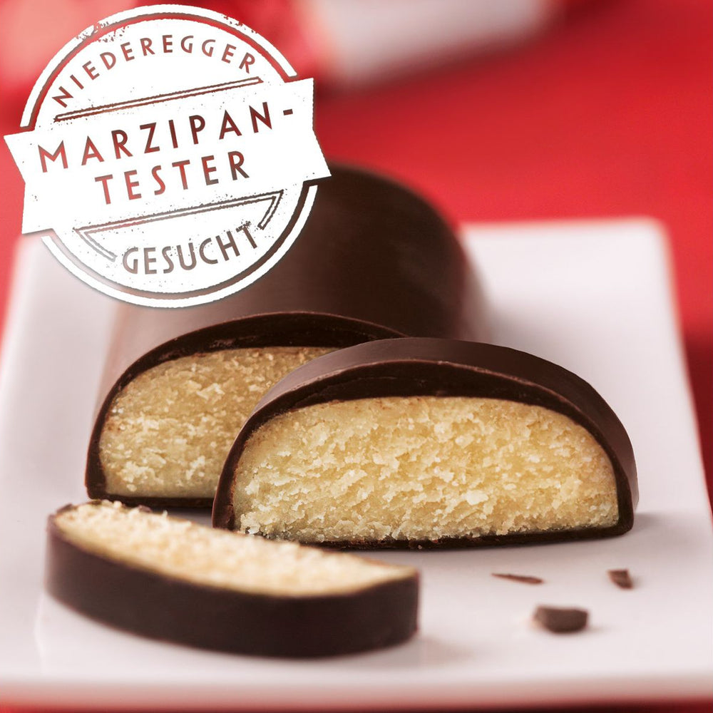 Marzipan tester with chocolate coating on a white plate against a red background, featuring Niederegger logo.