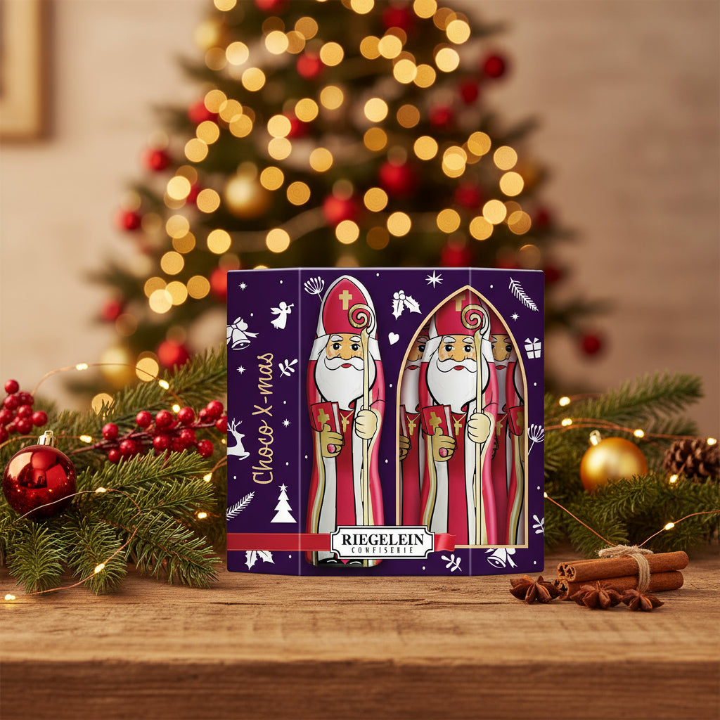 Purple Riegelein St. Nicholas chocolate gift box on a wooden table with evergreen branches and a lit Christmas tree