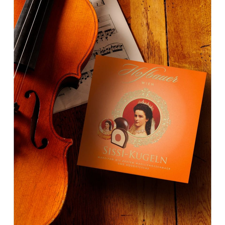 Hofbauer Sisi Pralines 200 g orange gift box displayed beside a violin