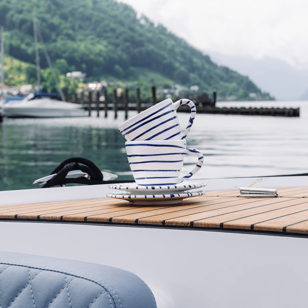 Blue striped Gmundner ceramic cups and saucers on a boat beside a lake
