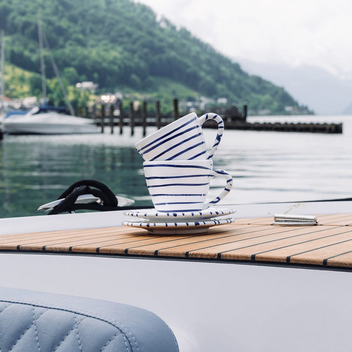 Blue striped Gmundner ceramic cups and saucers on a boat beside a lake