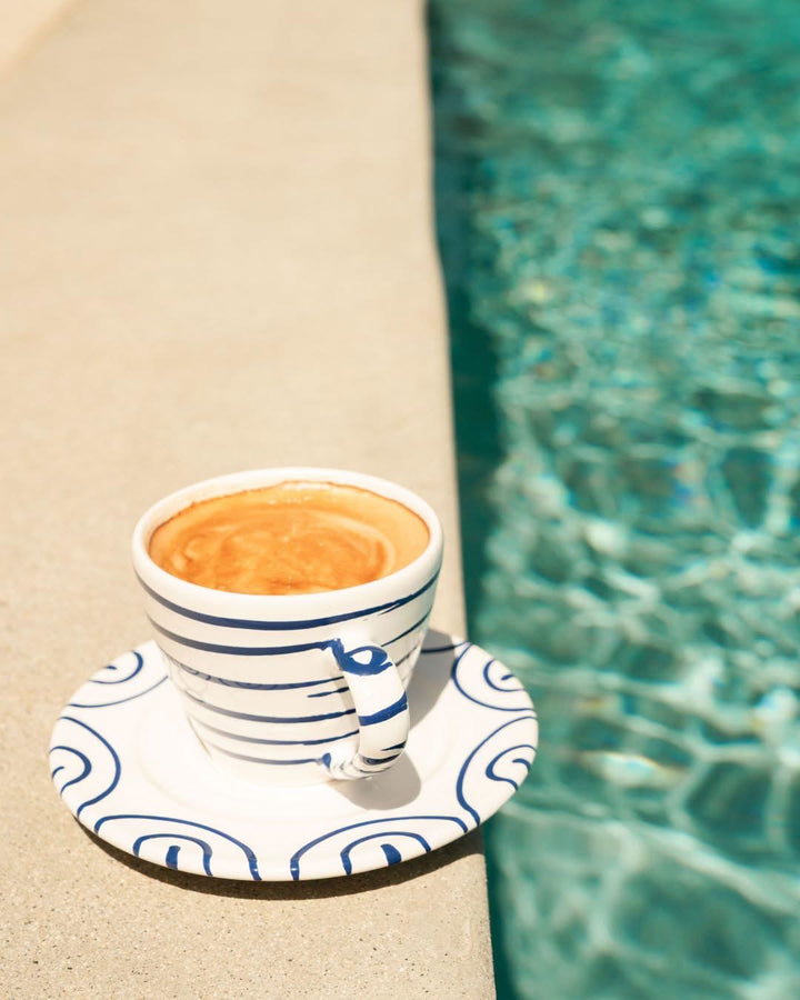 Blue flamed saucer paired with a striped coffee cup beside water; pieces sold separately