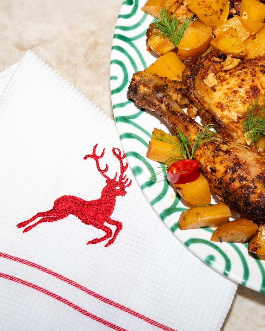 Ruby red deer embroidered tea towel beside a meal on green ceramic tableware
